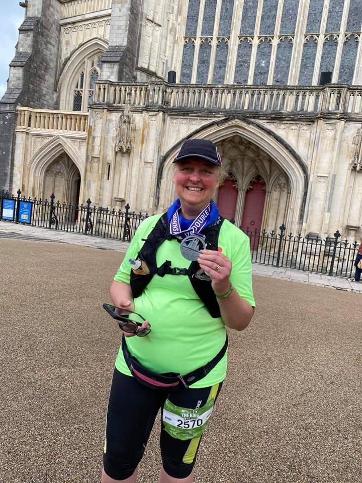 Carmen is hot and rosy-cheeked, standing in capri pants and a bright lime green t-shirt, proudly holding her finisher's medal in front of Winchester Cathedral. Her smile is broad